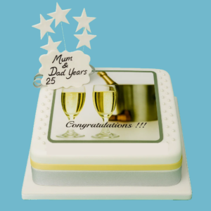 Champagne-themed celebration cake covered in smooth white fondant, decorated with an edible image of clinking champagne glasses and a cooler. Silver and gold ribbons wrap around the base, and a customisable message plaque sits on top.
