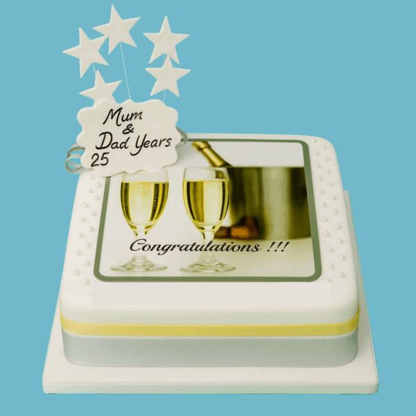 Champagne-themed celebration cake covered in smooth white fondant, decorated with an edible image of clinking champagne glasses and a cooler. Silver and gold ribbons wrap around the base, and a customisable message plaque sits on top.
