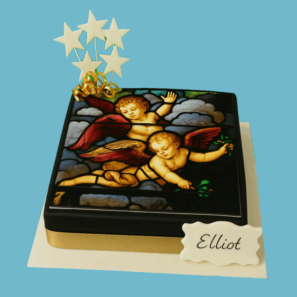 Round cake with dark icing, topped with a detailed edible image of a cherub in a stained glass style, finished with a golden ribbon around the base and small star decorations on top.