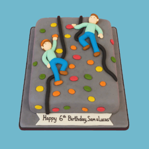 A cake designed to look like a grey climbing wall with a textured surface and brightly colored handholds scattered across it. Two fondant figures in climbing poses cling to the wall using black fondant ropes. A banner at the cake’s base displays a personalized message. The cake captures the excitement of rock climbing and is customizable in size and flavor for celebrations.