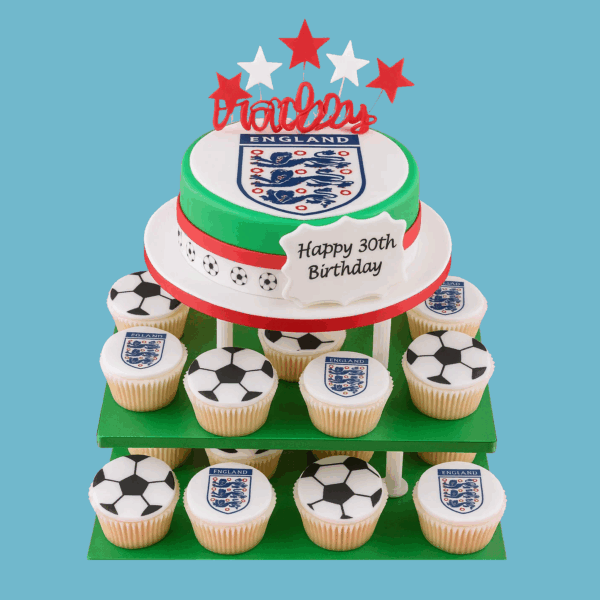 Football-themed cake and cupcake tower designed for England fans. The centre features a round cake with green and white fondant, topped with the England football emblem and wrapped in a red ribbon. Star toppers add a festive touch. Surrounding cupcakes display football-themed decorations in team colours and classic designs. A message plaque on the cake allows personalisation. The tower is customisable by flavour, sponge type, and cupcake quantity, making it ideal for birthdays, match-day parties, or football celebrations.