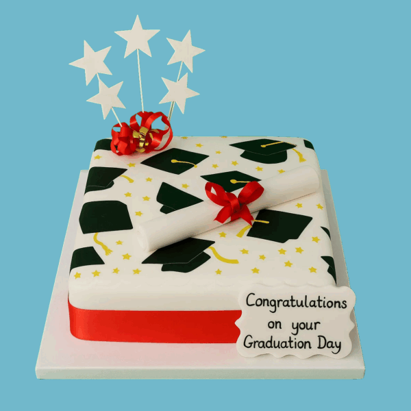 Elegant white fondant graduation cake with a bold red ribbon around the base, topped with a classic graduation cap decoration and a customizable message plaque for personalized congratulatory text.