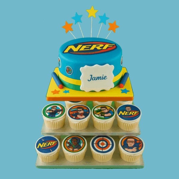 A vibrant Nerf-themed cupcake tower featuring a round cake on the top tier, decorated in bold blue and orange with the official Nerf logo. Below the cake, matching cupcakes are arranged in neat rows, each topped with colourful Nerf-inspired edible images such as darts, targets, and blasters. Star-shaped toppers and a customisable message plaque add a festive touch. The tower is visually striking, perfect for birthdays or themed parties, and designed for easy serving and transport.