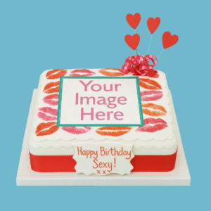 Square personalised photo cake with a central photo area, surrounded by bright red kiss print designs on a smooth white fondant surface. The cake features a scalloped edge, a red ribbon around the base, heart-shaped toppers, and soft pink ribbon decorations. A custom message plaque sits on top, offering space for personalised text. Ideal for special occasions like birthdays or anniversaries.