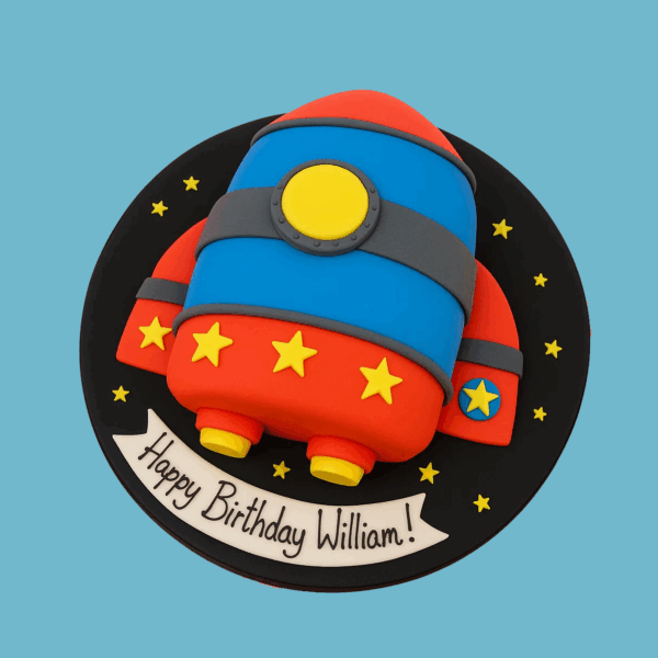 A round cake with a black fondant base decorated with small white dots resembling stars, topped with a novelty-shaped rocket ship. The rocket is brightly colored in red, blue, and grey, adorned with yellow and blue fondant stars. The design evokes a space theme, making it a vibrant and playful centerpiece for a space-themed party or celebration.