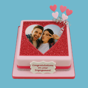 A romantic cake featuring a soft pink base wrapped with a rose gold ribbon. On top, a sparkling rose gold glitter heart frames a custom photo. The cake is decorated with heart-shaped toppers adding height and elegance. Below the photo heart, a plaque holds a personalized message. The overall design combines delicate pink tones and glittery rose gold accents, making it ideal for anniversaries, engagements, or Valentine’s Day celebrations.