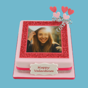 A Valentine’s Day cake with smooth pale pink fondant, decorated with a sparkling rose gold glitter frame around a central personal photo. The cake is wrapped with a matching pink ribbon at the base and topped with edible heart-shaped decorations. It includes a customizable edible message plaque and comes in various sizes and flavors, combining elegance and romance for a personalized celebration.