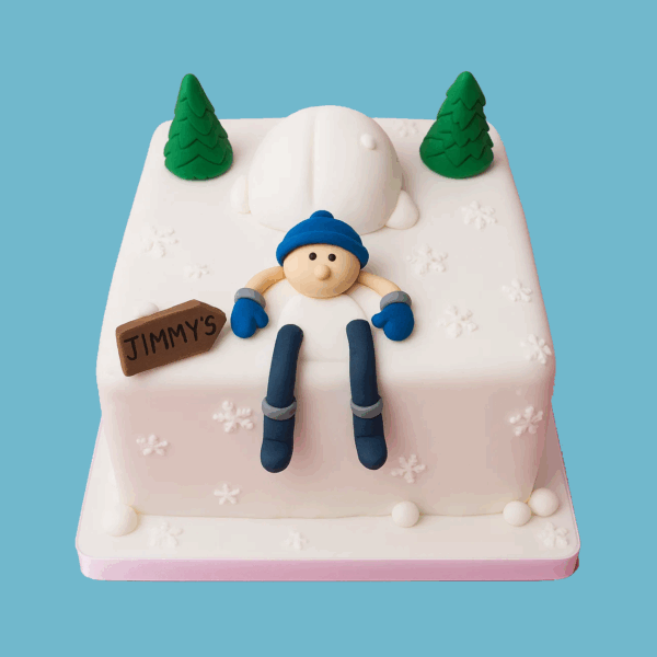 A square cake with smooth white fondant resembling fresh snow. On top, a detailed fondant skier wearing a bright blue hat and grey-blue ski suit is posed as if gliding down a slope. Surrounding the skier are several green fondant Christmas trees, creating a festive winter scene. The cake captures the energy of winter sports and holiday spirit.