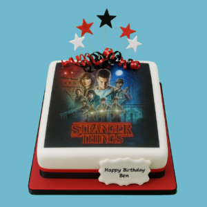 A square cake inspired by the TV series Stranger Things, featuring a detailed edible image with key characters and the show's iconic logo in vivid colors. The cake has a personalized message plaque on the front and star-shaped toppers on top, blending festive decorations with the show’s dark and thrilling theme. Designed as a centerpiece for fans, it combines striking visuals with ample servings for special occasions like birthdays or fan parties.