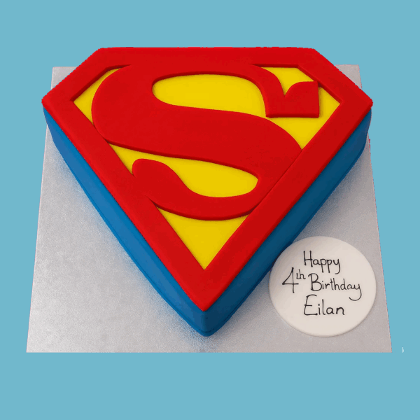 A cake shaped like the Superman shield logo, featuring a bold red "S" emblem set within a bright yellow diamond. The diamond is outlined with vivid red and blue borders, all resting on a sleek silver base. The cake has sharp, clean edges and smooth fondant for a polished, vibrant finish, making it a striking centerpiece for superhero-themed celebrations.