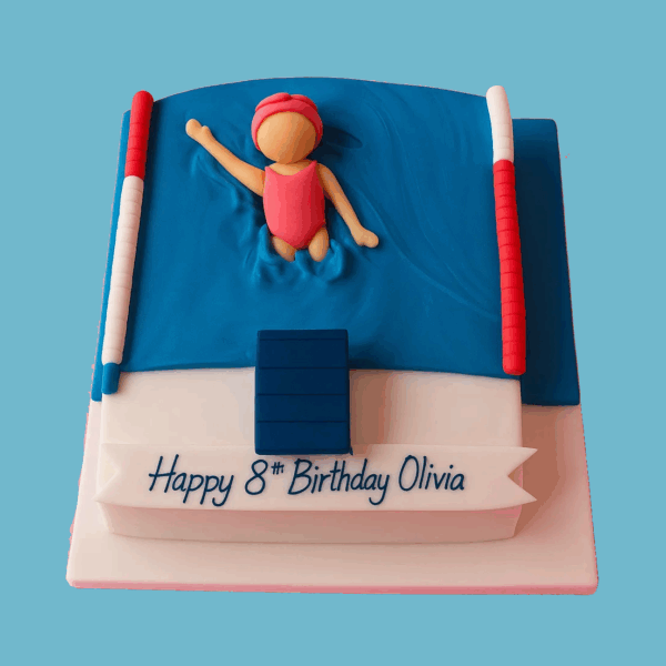 A rectangular Swimming Pool cake with smooth blue fondant mimicking sparkling water, featuring a fondant swimmer in a bright pink swimsuit and matching cap poised to dive. White and red lane markers line both sides of the pool, and a blue starting block sits at one end. The cake’s detailed decoration creates a realistic and lively swimming pool scene, perfect for celebrations involving swimmers or pool parties.
