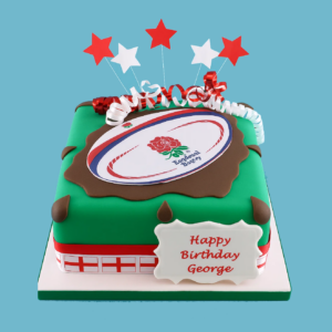 England rugby team cake featuring a rugby ball with the red rose logo on a green base, surrounded by red and white stars, ribbons, and a St. George’s Cross border.